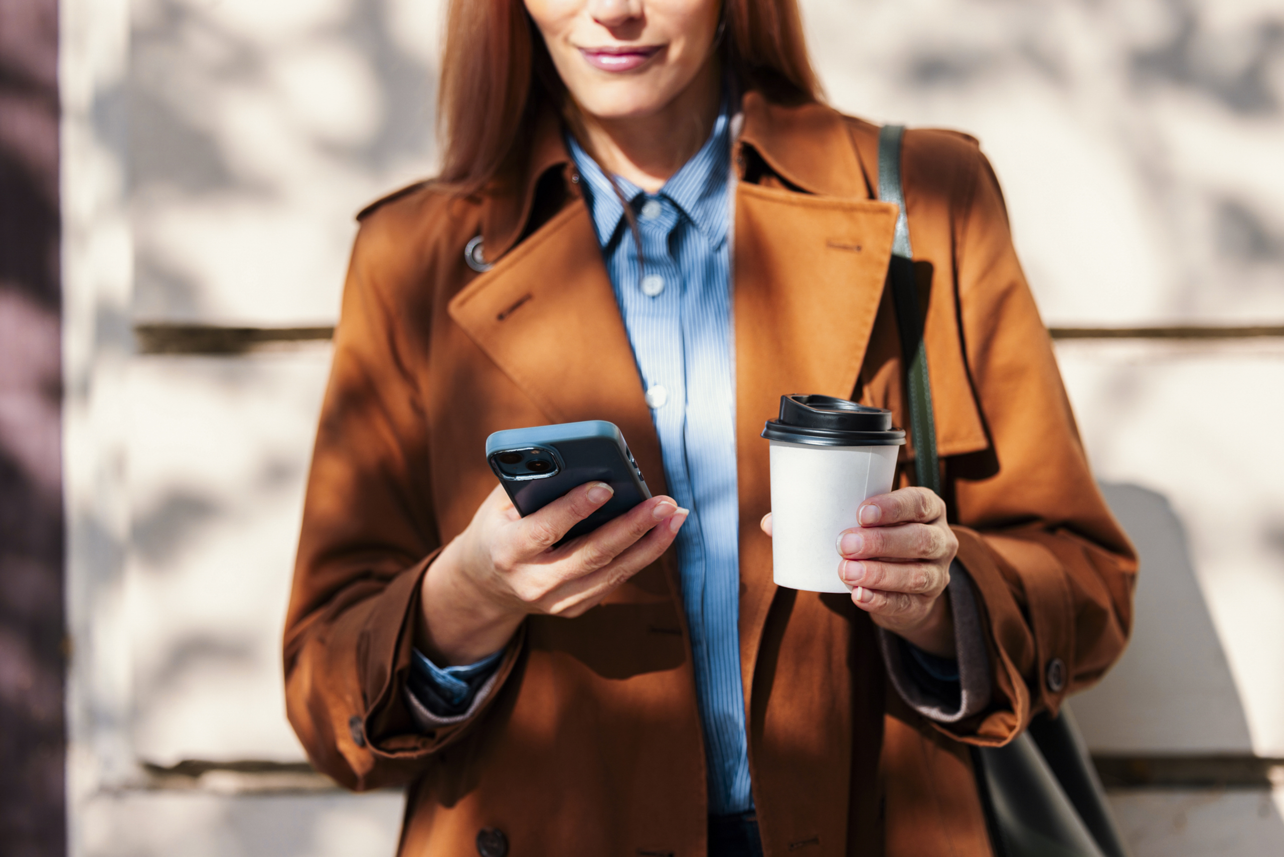 A woman uses her phone on the go whilst drinking a take out coffee